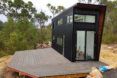 A black tiny home with a deck.