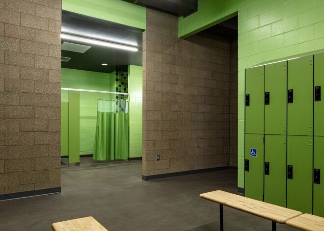 A green locker room with benches lined in front of the lockers