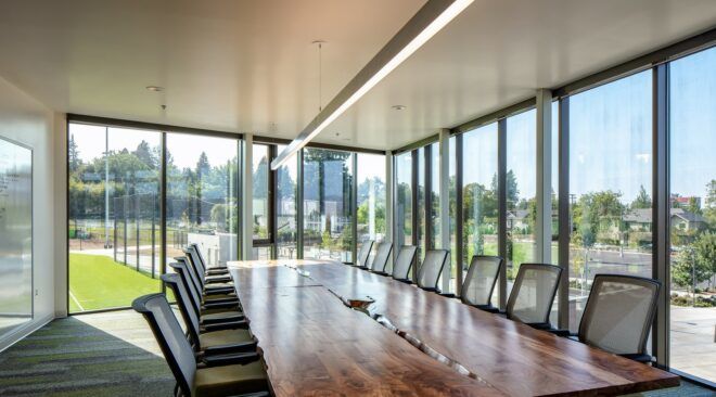 A meeting room with a long rectangle table and chairs pushed on either side of it with windows all around