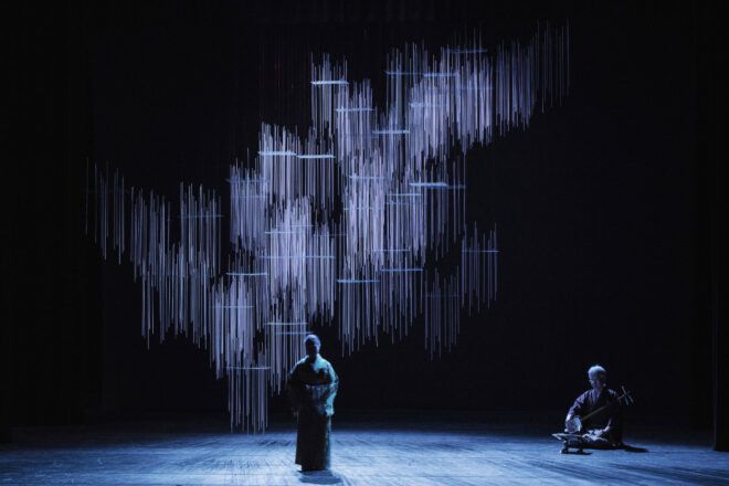 Traditional Japanese performance taking place on the stage lit up by the installation made of scrap wood.