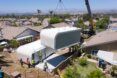 A crane lifting a house that looks like a shipping container into an suburban neighborhood