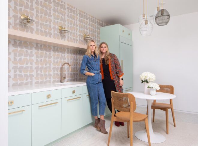 Two blonde women standing close together in a kitchen space