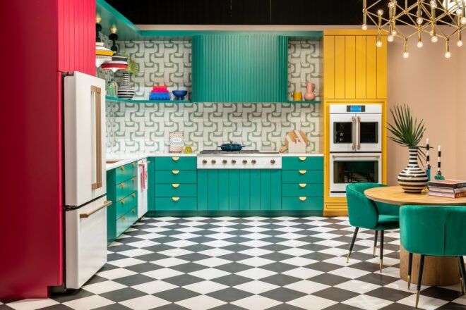 A colorful room with teal kitchen counter tops and cupboards above, a yellow wall where the oven is against the wall, and a red strip where the fridge is on the left-hand side with checkered tiles