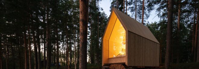 A pointed house structure with its light on in the middle of a forest