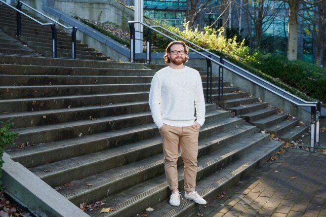 A white man wearing a white shirt and khaki pants, standing on stone steps