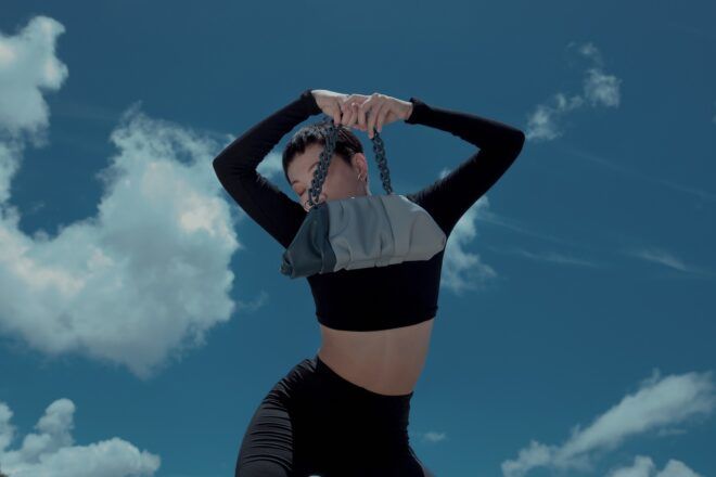A woman wearing a crop top black long sleeve and black leggings holds a blue purse in front of her face