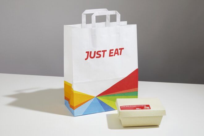 A to-go bag that reads "just eat" with a to-go box in front of it