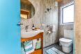 A bathroom with a white toilet, a wooden wink with a white porcelain bowl and a circle mirror above it