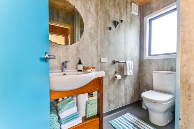 A bathroom with a white toilet, a wooden wink with a white porcelain bowl and a circle mirror above it