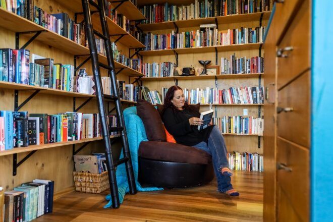 A woman sits in a brown chair in a corner with the walls lined in shelves of books