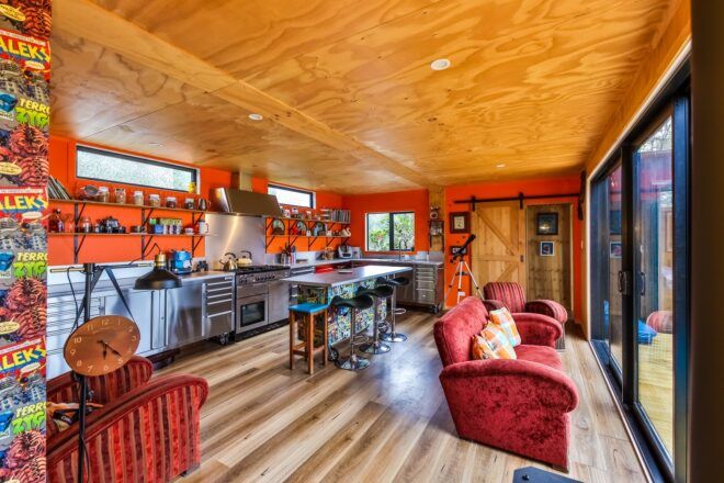 A couch is in front of a kitchen area with orange walls and wooden ceiling