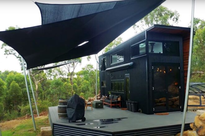 A black tiny home with a deck.