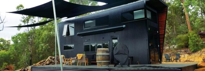 A black tiny home with a deck.