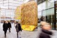 A straw-covered structure sits in a walk area filled with pedestrians