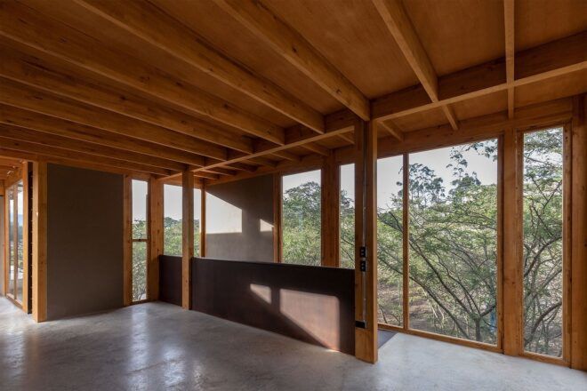 A room with a wooden area that covers the staircase and floor-to-ceiling windows of views of the forest