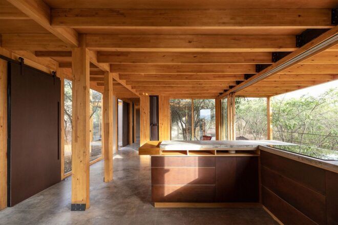 A living room with exposed wooden ceiling beams and a 360 viewing of the forest outside