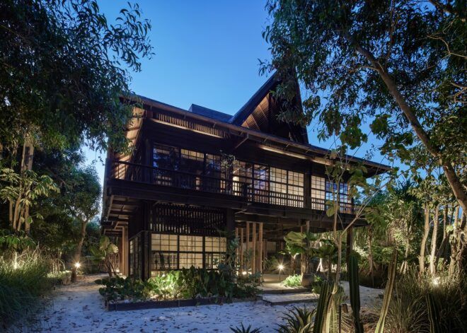 A wooden three story house called The Barn by Alexis Dornier lights up from inside during an evening day