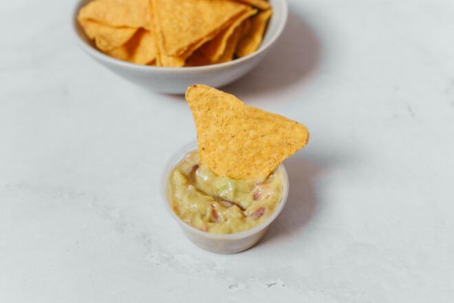 A bowl of chips sits behind a chip dipped in a small sauce bowl