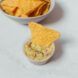 A bowl of chips sits behind a chip dipped in a small sauce bowl