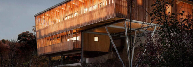 Night view of a two-story wood house suspended off a hill