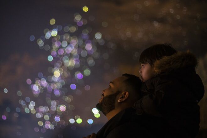 A man with a kid on his shoulders staring up at the night sky