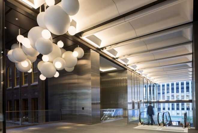 The top of an escalator has a hanging orb light installation