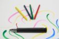A single black pen in front of yellow, blue, green and red colored pencils