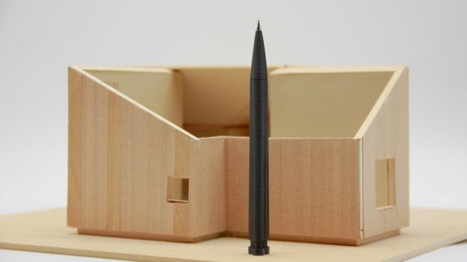 A black pen standing upright in front of wooden office compartment holder for pencils and pens
