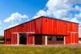 A red barn in the middle of a field on a clear blue sky with white clouds day