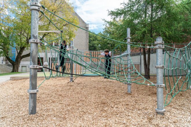Two kids playing on a jungle gym in a playground that has ropes suspended above the ground