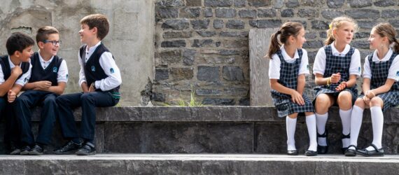 Three boys sitting sitting to the left and three girls sitting to the right on stone steps
