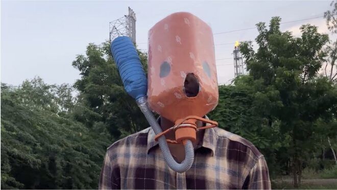 A person wearing an orange gas container over his head with a blue nozzle attached to it