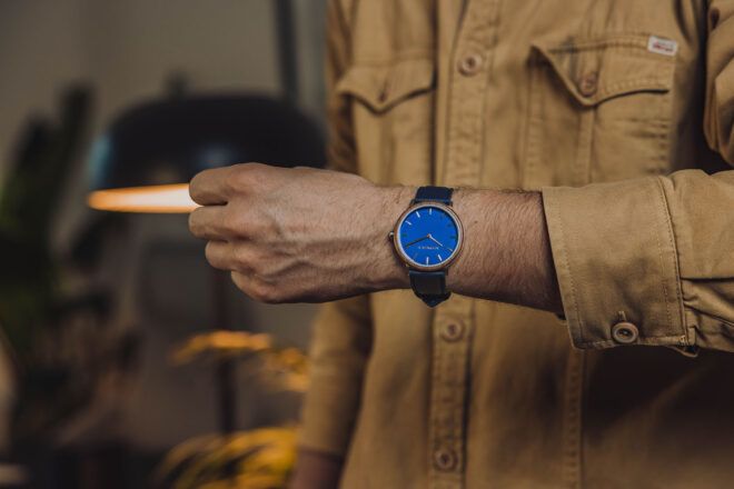 A watch with a bleu face on a person's wrist.