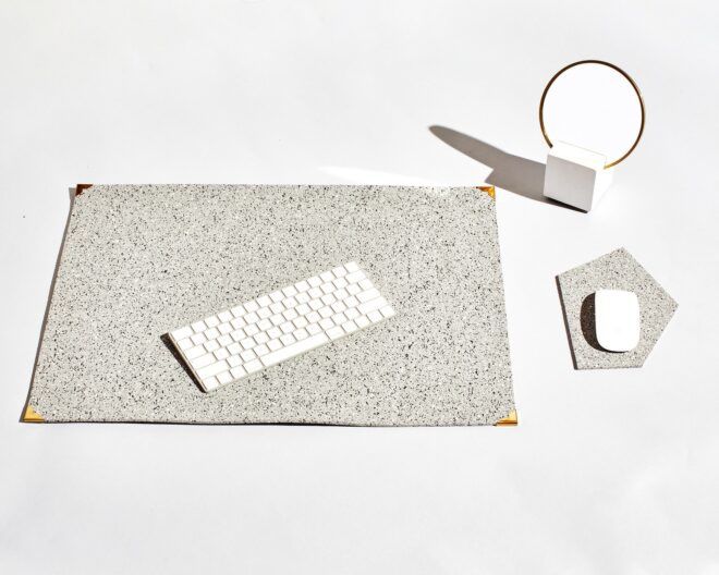 A laptop mat with a white keyboard on top of it, a mirror of the corner of it and a mouse on top of a grey mousepad