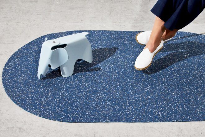 A blue playmat with a light blue elephant structure on top of it and a persons legs wearing white shoes dangling over the mat