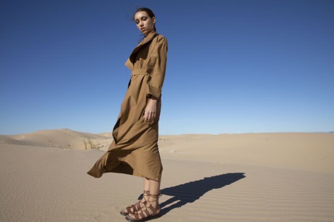 A woman standing in a desert with a brown trench coat and brown scandals