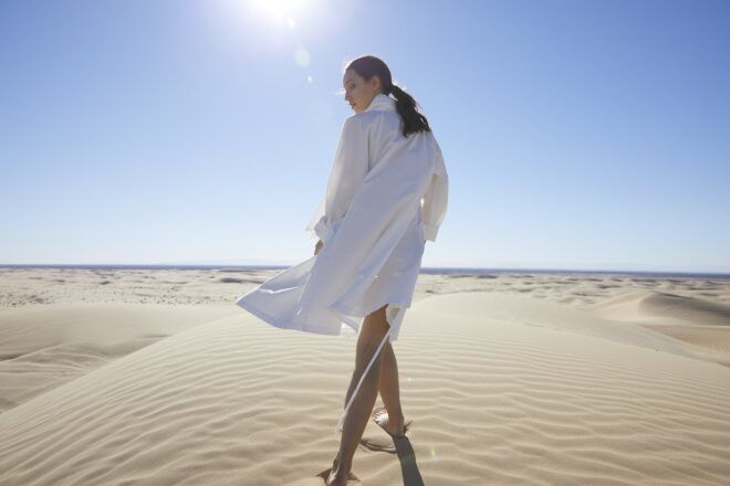 A the back of a woman wearing a white trench coat in the middle of a desert