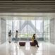 A lounge area where people sit and talk by a wall of windows.
