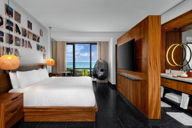 A guestroom with a large white bed facing a TV mounted on a wall with photo behind it