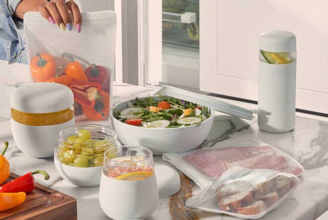 A kitchen island table spread with a bowl of salad, Tupperware and reusable zip locks