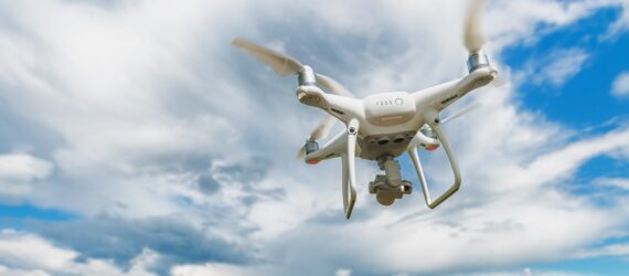 A flying white drone across a blue sky with white clouds