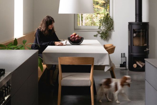 Woman sitting in the dining space with a bowl of apples on the table, while a dog moves out of the image frame