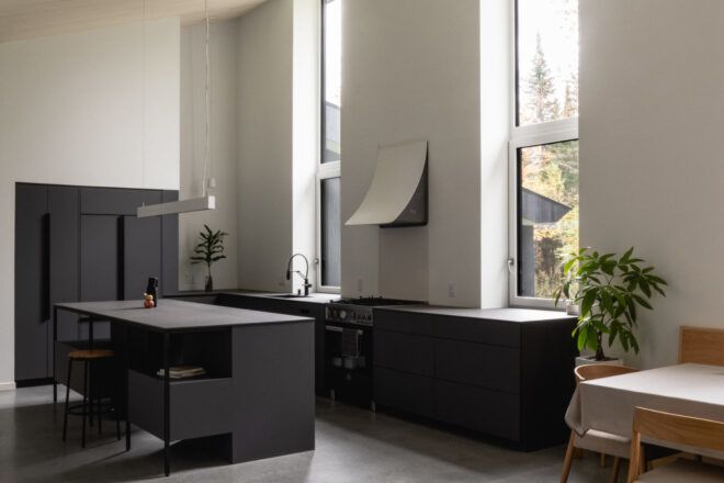View towards the kitchen with dark appliances, high ceilings, and tall rectangular windows
