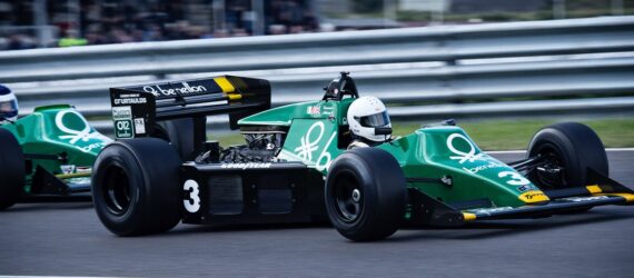 Two green racing cars lined up one in front of the other on a race car track