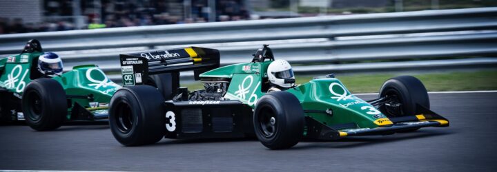 Two green racing cars lined up one in front of the other on a race car track