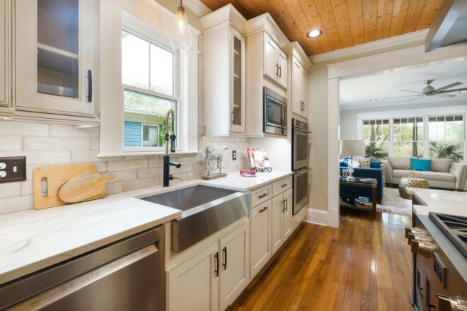 A kitchen with white countertops and stainless steal dishwasher and sink with wooden floors