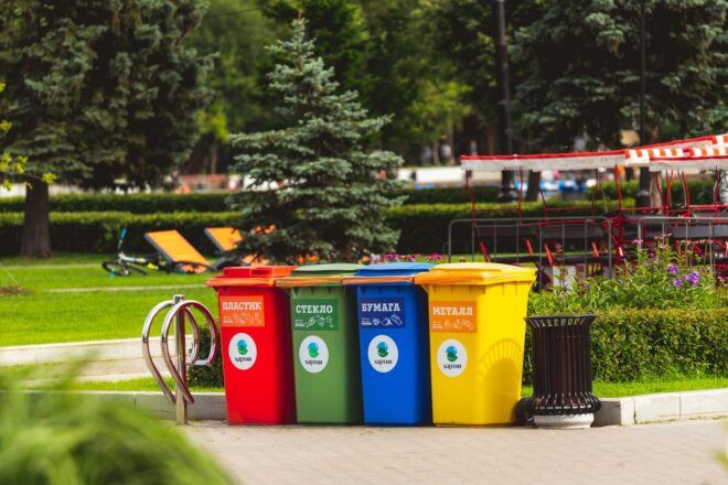 Four bins in red, green, blue and yellow colors. They sit on the pavement in a park