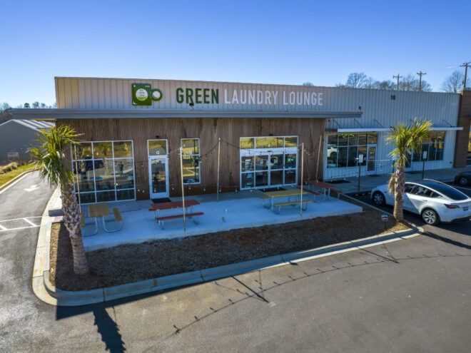 Exterior view of the Green Laundry Lounge with decorative hanging string lights and colorful picnic tables