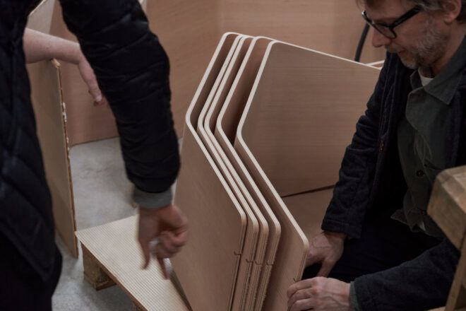 Two people holding sheets of wood cut out in different shapes