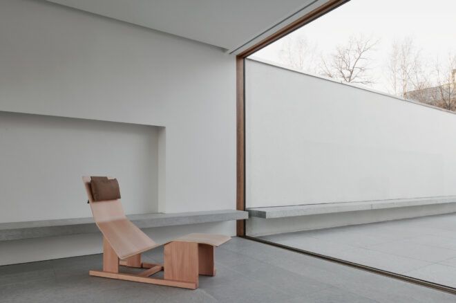 A wooden chaise lounge chair sitting behind a large glass window